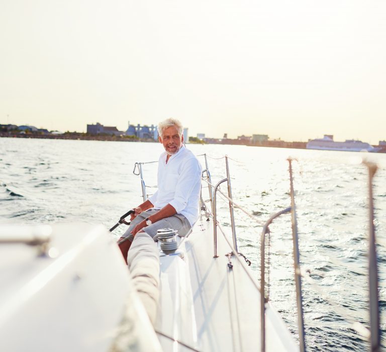 Mature man steering the rudder of his boat while out for a sail along the coast on a sunny day