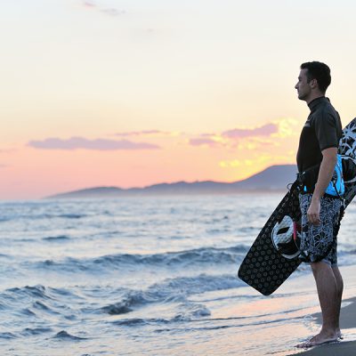 Portrait of a strong young surf man at beach on sunset in a contemplative mood with a surfboard