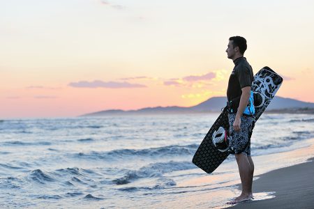 Portrait of a strong young surf man at beach on sunset in a contemplative mood with a surfboard